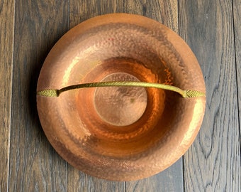 May include: A hammered copper bowl with a gold-toned handle. The bowl has a slightly rounded shape and a textured surface.