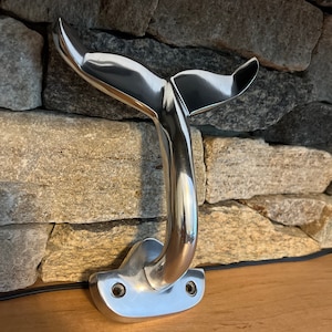 May include: A silver whale tail shaped wall hook. The hook is mounted on a wooden surface.