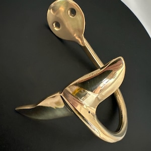 May include: A gold-colored metal hook shaped like a dolphin fin. The hook has two holes on the top for hanging.