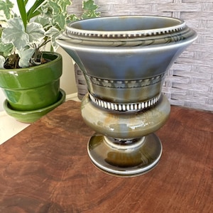 May include: A decorative ceramic vase with a wide, flared top and a bulbous base. The vase features a two-tone color scheme of blue and green with white accents. The vase is approximately 10 inches tall.