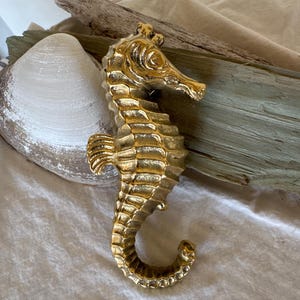 May include: A gold-colored metal seahorse figurine with a detailed design. The figurine is sitting on a piece of driftwood.