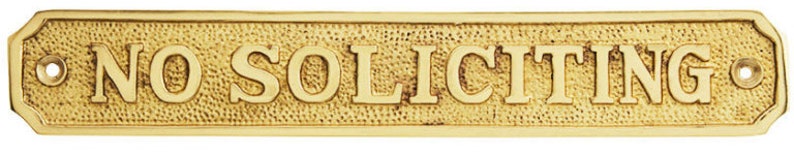 May include: A rectangular brass sign with the words "NO SOLICITING" in bold, raised letters. The sign has a textured background and decorative edges, with holes for mounting.