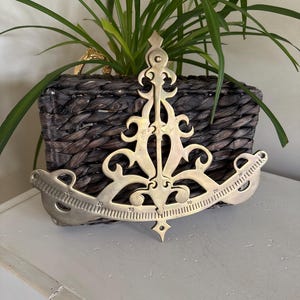 May include: A gold-toned metal protractor with an ornate design. The protractor has markings from 0 to 30 degrees.