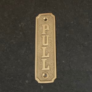 May include: A brass door pull with the word "PULL" engraved in a vertical orientation.