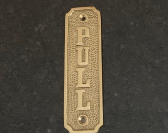 May include: A brass door pull with the word "PULL" engraved in a vertical orientation.