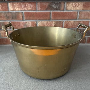 May include: A large, antique brass planter with two handles. The planter is round and has a smooth, polished surface.
