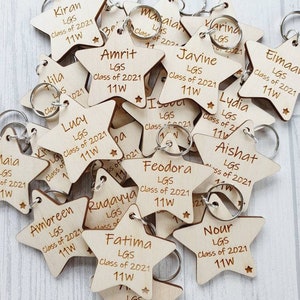Peut inclure: Un tas de porte-cl&eacute;s en forme d'&eacute;toile en bois avec des noms grav&eacute;s et le texte "LGS Class of 2021 11W".