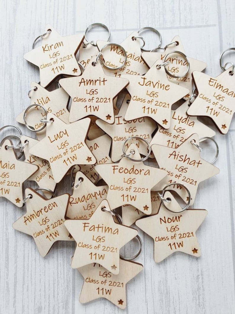 Peut inclure: Un tas de porte-cl&eacute;s en forme d'&eacute;toile en bois avec des noms grav&eacute;s et le texte "LGS Class of 2021 11W".