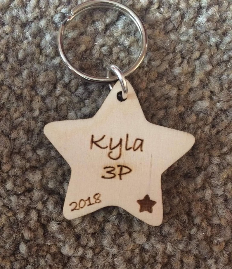 Peut inclure: Un porte-cl&eacute;s en bois en forme d'&eacute;toile avec le nom "Kyla 3P 2018" grav&eacute; dessus.