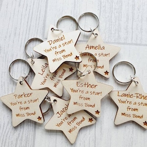 Peut inclure: Un ensemble de huit porte-cl&eacute;s en bois en forme d'&eacute;toile avec le texte "You're a star! from Miss Bond" et le nom d'un enfant sur chaque porte-cl&eacute;s.