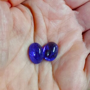 Puede incluir: Dos piedras ovaladas de vidrio azul oscuro. Las piedras son lisas y brillantes.