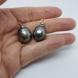 Op de afbeelding: Twee donkergrijze traanvormige parels met zilveren springringen. De parels hangen aan de springringen.