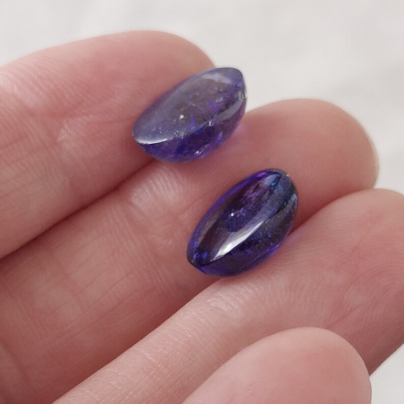 Puede incluir: Dos piedras preciosas ovaladas facetadas de color p&uacute;rpura con un tono azul.