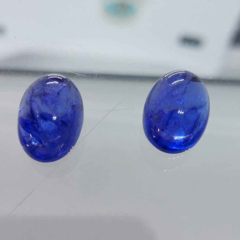 Puede incluir: Dos piedras preciosas azules de forma ovalada con un aspecto ligeramente nublado.