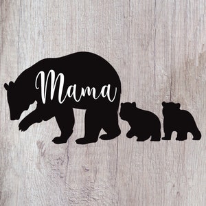 Puede incluir: Silueta negra de una osa madre con la palabra "Mama" escrita en su espalda, seguida de dos ositos m&aacute;s peque&ntilde;os. La imagen est&aacute; sobre un fondo de madera.
