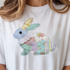 May include: White t-shirt featuring a patchwork bunny design. The bunny is composed of various fabric patterns, including floral, gingham, and polka dots, in pastel colors. The design includes a ruffled collar and a black button eye. The shirt is a casual, oversized fit.