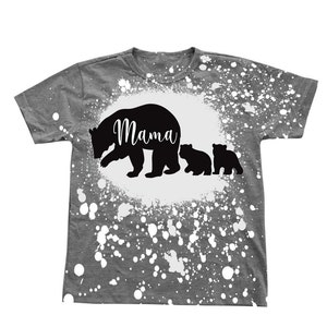 Puede incluir: Camiseta gris con un dise&ntilde;o de pintura salpicada blanca. La camiseta presenta una silueta negra de una osa madre y dos cachorros con la palabra "Mama" escrita en la espalda de la osa madre.