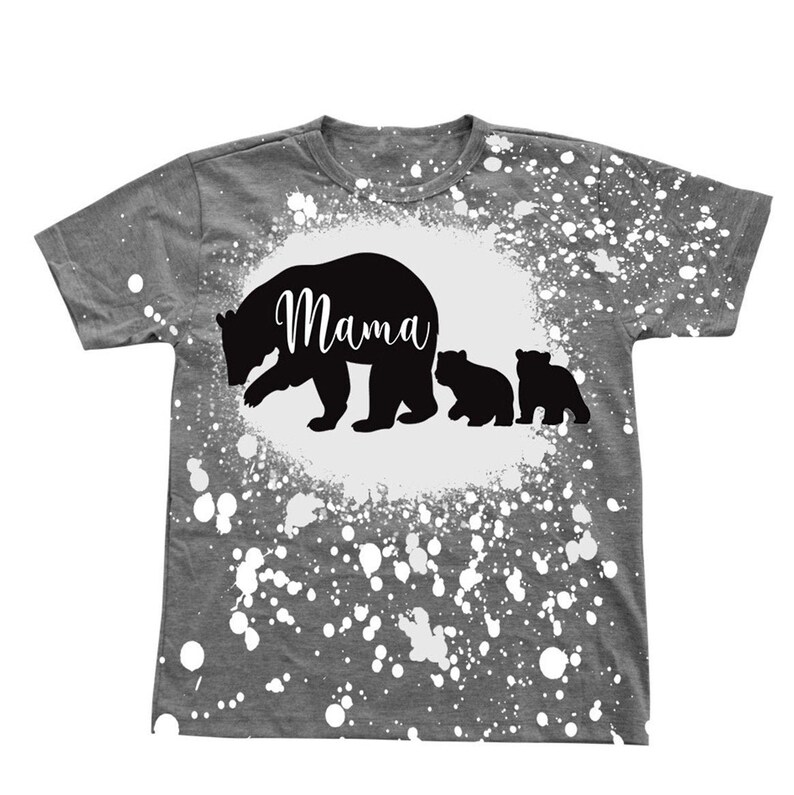 Puede incluir: Camiseta gris con un dise&ntilde;o de pintura salpicada blanca. La camiseta presenta una silueta negra de una osa madre y dos cachorros con la palabra "Mama" escrita en la espalda de la osa madre.