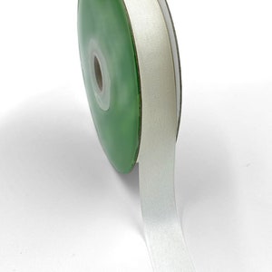 May include: A spool of white satin ribbon with a green plastic bobbin.