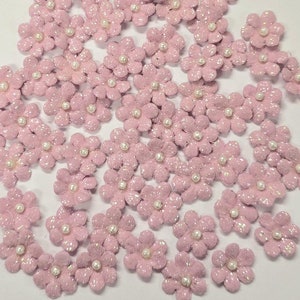 May include: A large quantity of small pink glitter flowers with a pearl center. The flowers are scattered on a white background.