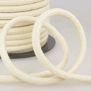 May include: A close-up of a reel of natural white cotton cord. The cord is braided and has a smooth texture.