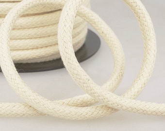 May include: A close-up of a reel of natural white cotton cord. The cord is braided and has a smooth texture.
