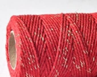 May include: A spool of red twine with gold glitter accents. The twine is wound tightly around a cardboard tube.