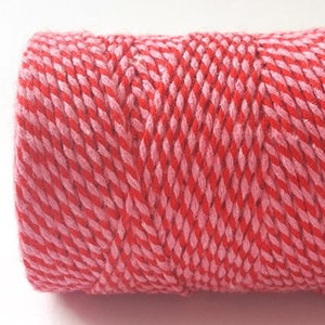 Könnte beinhalten: Eine Rolle Backgarn in Rot und Rosa. Das Garn ist verdreht, um ein gestreiftes Muster zu erzeugen.