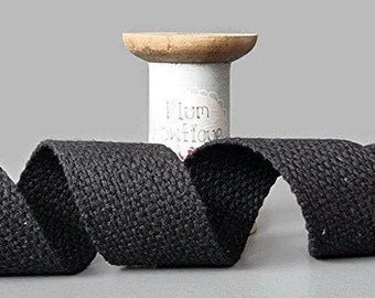 Puede incluir: Cinta de algodón negra, de aproximadamente 2,5 cm de ancho, enrollada alrededor de un carrete de madera. La cinta es un tejido tejido con una superficie texturizada.