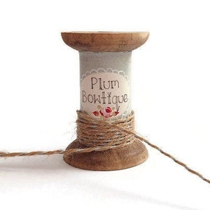 Könnte beinhalten: Eine Holzspule mit einem Etikett mit der Aufschrift "Plum Boutique" und umwickelt mit Schnur. Die Schnur ist braun und teilweise von der Spule abgewickelt.