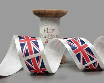May include: White satin ribbon with a repeating pattern of the Union Jack flag. The ribbon is coiled on a spool labeled "Plum Bowtique."