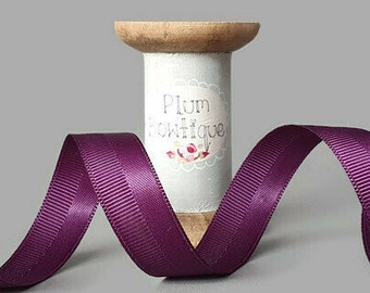 May include: A spool of deep purple satin ribbon with a white label that reads "Plum Boutique".