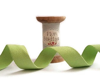May include: A spool of green cotton twill ribbon with a label that reads "Plum Bowtique".