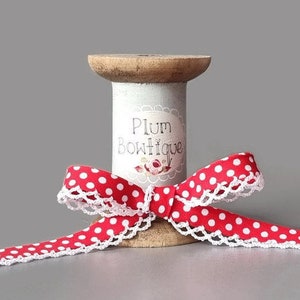 May include: Red and white polka dot ribbon with white lace trim wound around a wooden spool. The spool has a label that reads "Plum Bowtique".