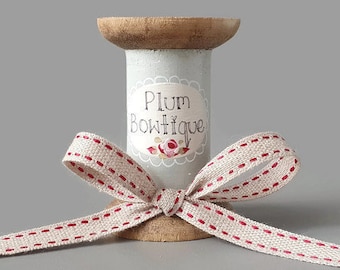 May include: A wooden spool with a white label that says "Plum Boutique" and a red and white ribbon tied around it.