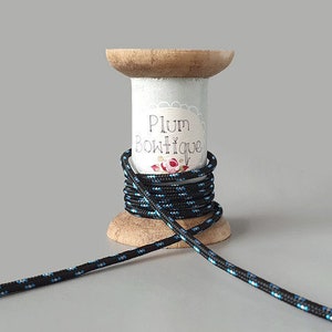 Puede incluir: Una bobina de cordón negro y azul con una etiqueta blanca que dice "Plum Boutique" en una bobina de madera.