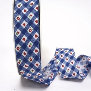 May include: Blue and white gingham ribbon with red hearts and flowers. The ribbon is rolled up on a spool.