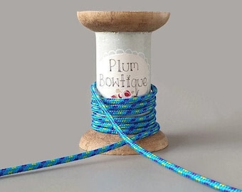 Op de afbeelding: Een spoel met blauwe, groene en paarse koord met een wit label waarop "Plum Boutique" staat.