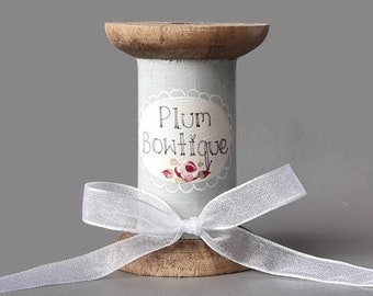 May include: A wooden spool with a light blue and white label that says "Plum Boutique" and a white ribbon tied around it.