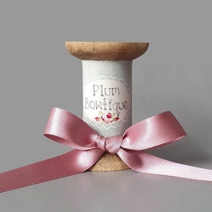 May include: A wooden spool with a pink satin ribbon tied around it. The spool is labelled "Plum Boutique".