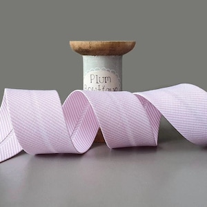 Puede incluir: Cinta de rayas rosa y blancas enrollada alrededor de un carrete de madera. El carrete tiene una etiqueta que dice "Plum Boutique".