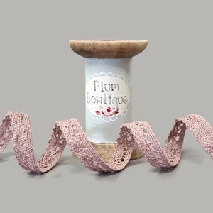 May include: A spool of dusty pink crochet lace trim with a white label that reads "Plum Boutique".