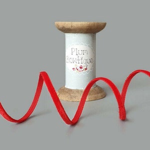 May include: Red velvet ribbon wound around a wooden spool with a label that reads "Plum Boutique".