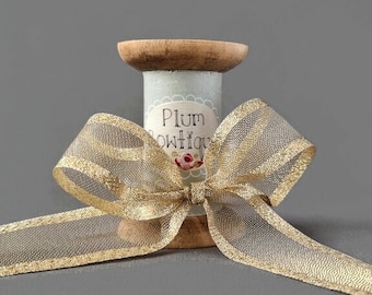 May include: A wooden spool with a blue and white patterned label that says "Plum Boutique" is tied with a gold ribbon bow.