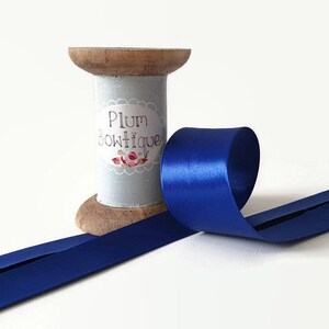 May include: A spool of royal blue satin ribbon with a wooden base. The spool is labelled "Plum Boutique".