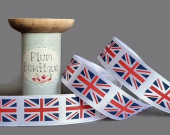 May include: White satin ribbon with a repeating pattern of the Union Jack flag in red, white, and blue. The ribbon is wound around a wooden spool labeled "Plum Boutique".