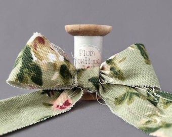 May include: A spool of green and white floral patterned fabric ribbon with a label that reads "Plum Boutique".