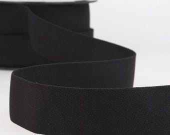 Puede incluir: Un rollo de cinta elástica negra. La cinta está desenrollada, revelando una superficie texturizada y una forma suave y flexible. La cinta se utiliza probablemente para coser, manualidades o confección de prendas.