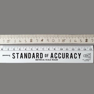 Puede incluir: Una regla blanca con marcas negras y el texto "STANDARD OF ACCURACY" y "METRICAL SCALE RULER". La regla mide 15 cm de largo y tiene un logotipo de penco.