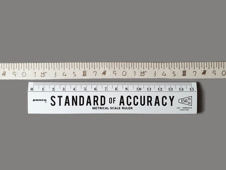 Puede incluir: Una regla blanca con marcas negras y el texto "STANDARD OF ACCURACY" y "METRICAL SCALE RULER". La regla mide 15 cm de largo y tiene un logotipo de penco.
